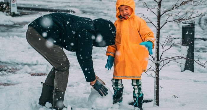 child in the snow with parent making snow ball