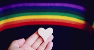 white hand holding a heart under a painted rainbow