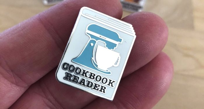 image of an enamel pin with a stand mixer design and the words "cookbook reader"