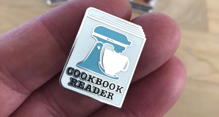 image of an enamel pin with a stand mixer design and the words "cookbook reader"