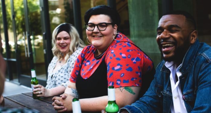 two women and a man drinking beers at a long wooden table outdoors https://unsplash.com/photos/aCEg6DQEiDo