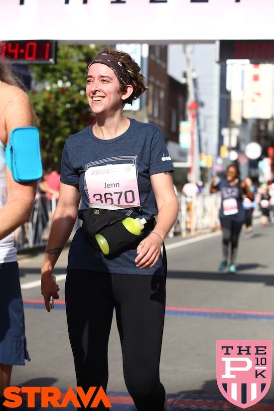 a photo from the Philly 10K of a smiling Jenn in running gear, just crossing the finish line; photo credit Jenn Northington