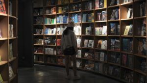 woman browsing in a dark bookstore surrounded by books and bookshelves