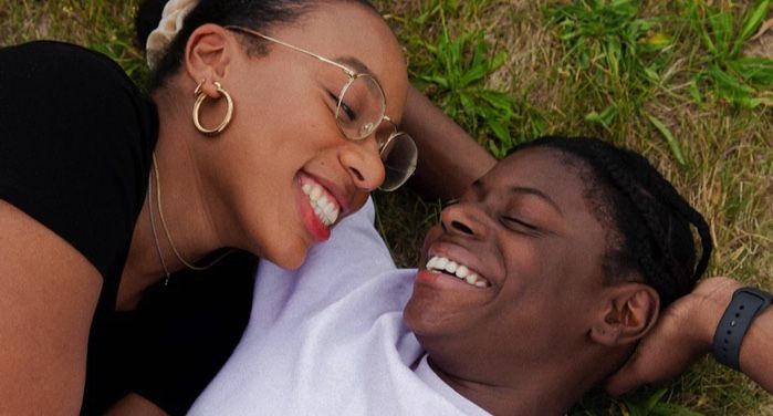 two Black women embracing while lying in grass