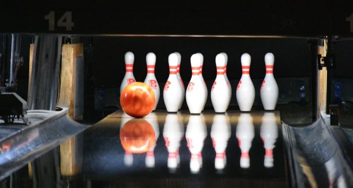 orange bowling ball speeding towards bowling pins