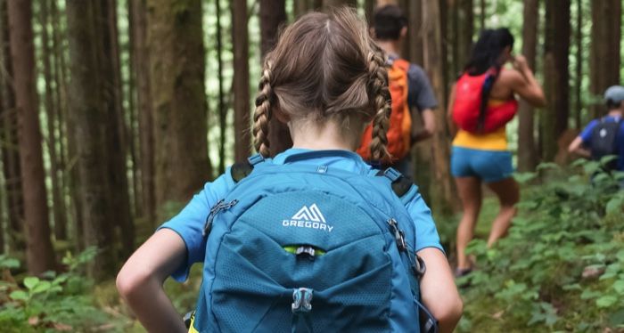 view of child's back as she hikes through the woods on a trail