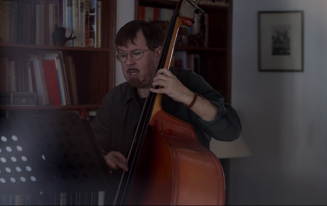 Higgins plays bass in front of his bookcase