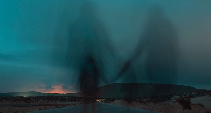 ghostly image of two people holding hands at sunset