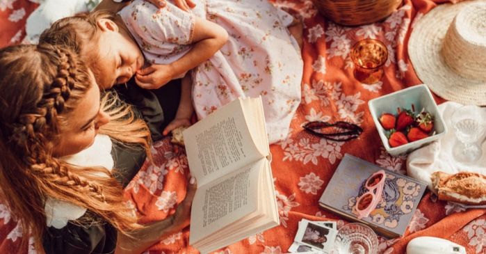 mother or parent reading to child or daughter on a picnic blanket