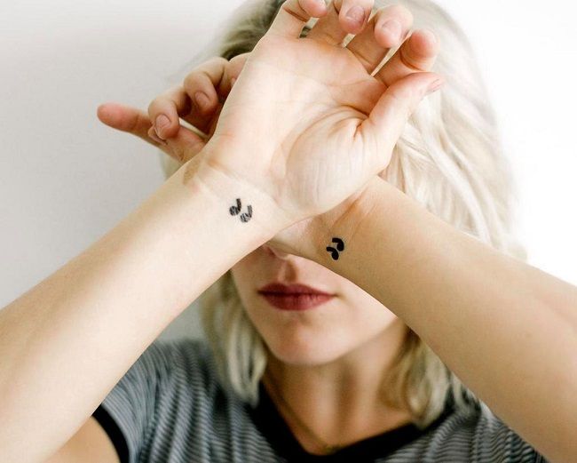Image of person with quotation mark temporary tattoos on each of their wrists and their arms are crossed in front of their face