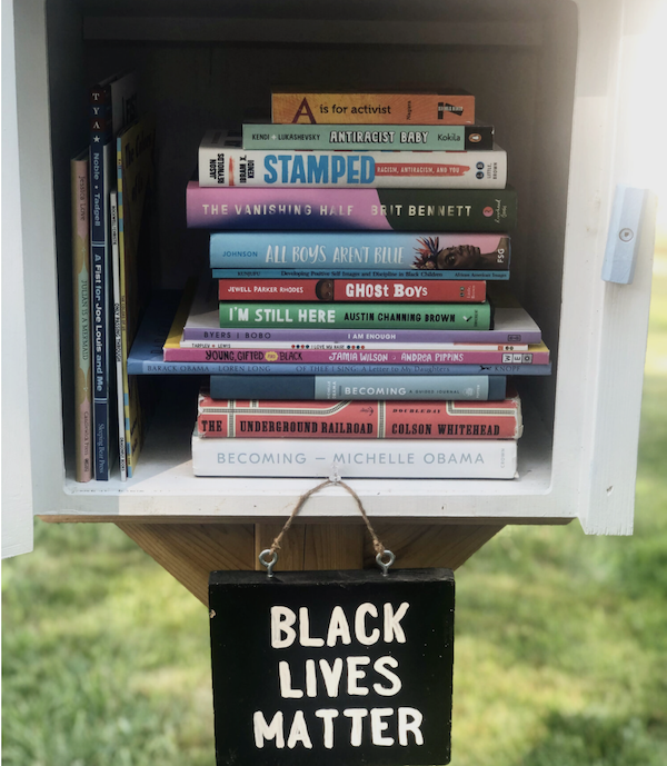 Image of a Little Free Library with a stack of diverse books and a sign reading 