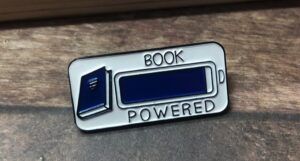 image of a blue and white "book powered" enamel pin. Design features a book next to a battery life indicator