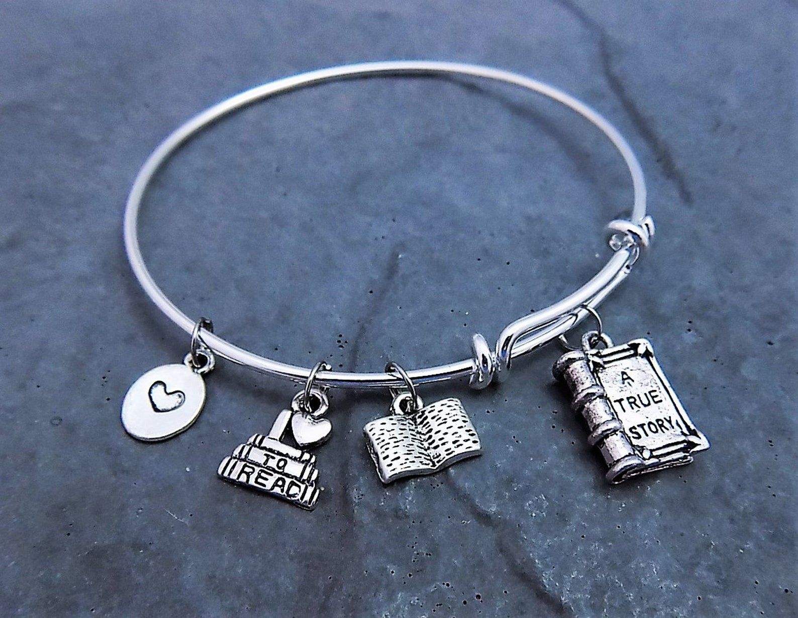 a silver booklover charm bracelet with four charms: a heart, a smalll book stack, en open book, ad a closed book without that reads: a true story