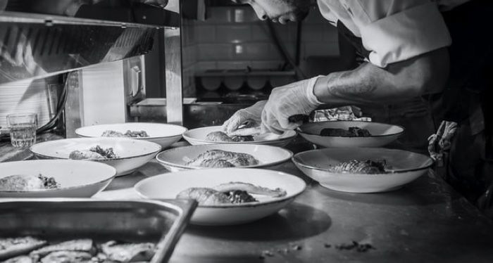 chef bends over to garnish dishes in black and white picture