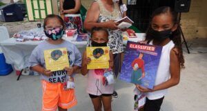 Three brown-skinned Indigenous children hold books from the Little Free Library opening ceremony. Image provided by Little Free Library.