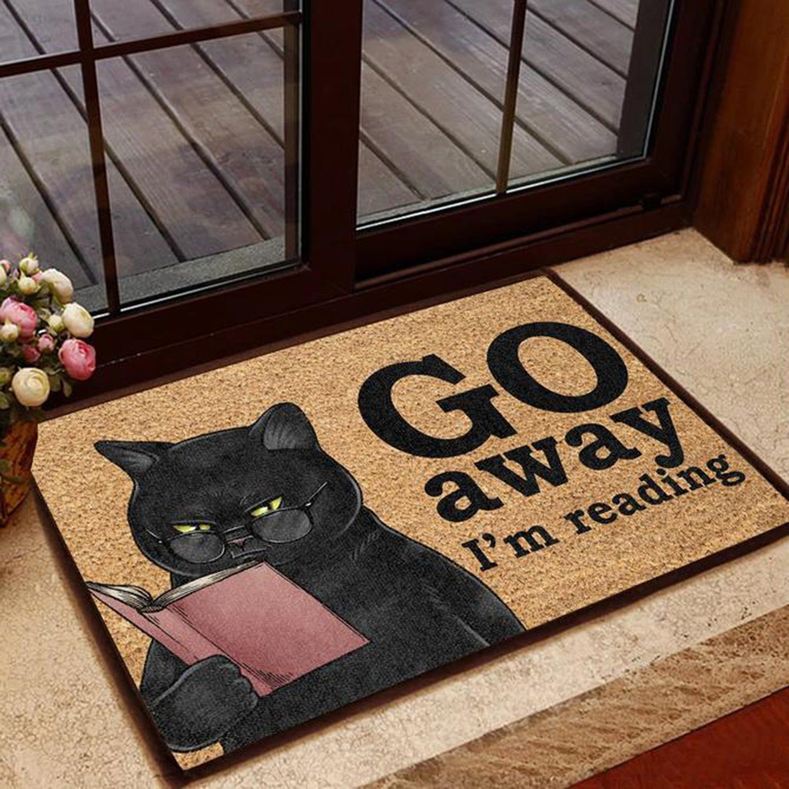 Image of a black cat reading a book with the text "Go away I'm reading" on a brown doormat. 