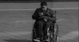 image of grayscale guy sits in wheelchair looking at cell phone