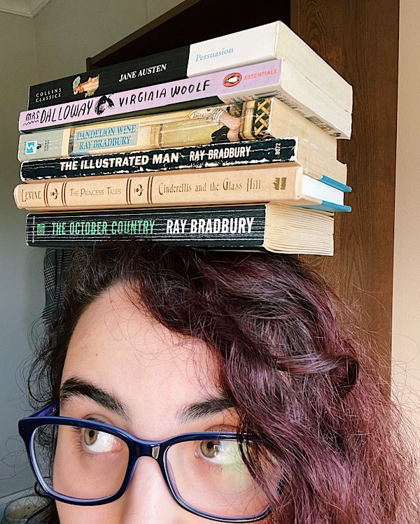 Up-close of a woman wearing glasses, with books stacked on her head