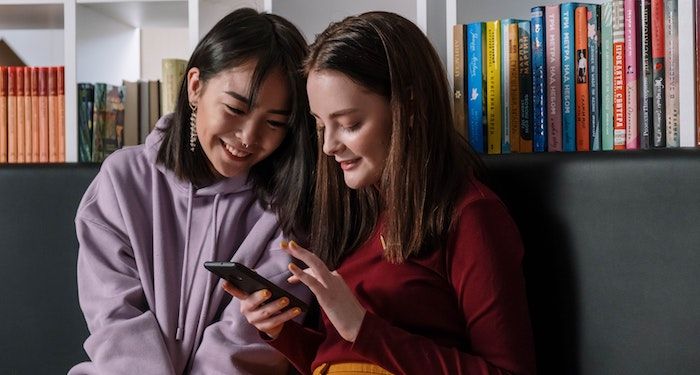 teenage girls in library looking at phone together