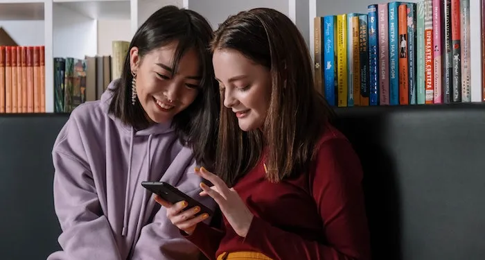 teenage girls in library looking at phone together