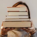 a photo of a person obscuring their face with a stack of books