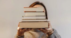 a photo of a person obscuring their face with a stack of books