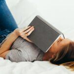 a photo of a woman reading in bed holding a book over her face