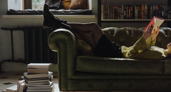 woman reading on couch with stack of books