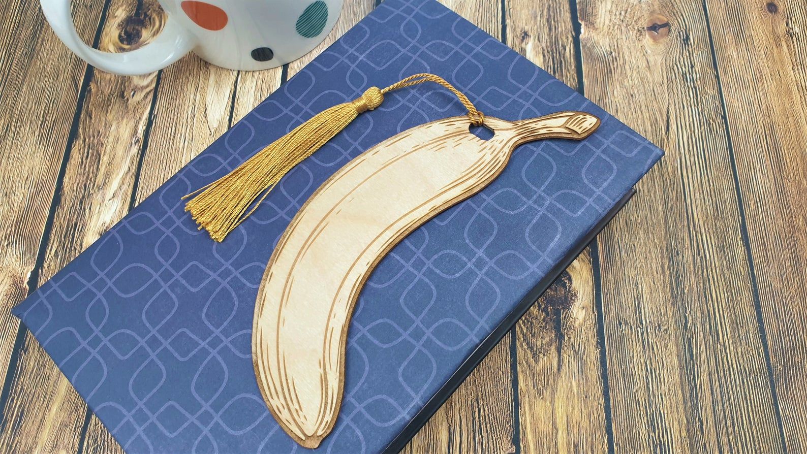 Image of a wooden, engraved banana bookmark on top of a blue ereader cover. 