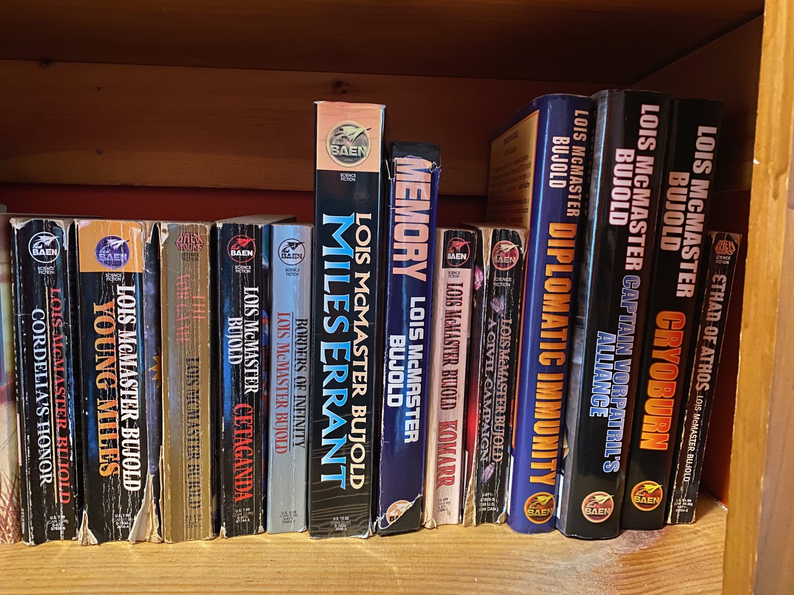 The books in the Vorkosigan Saga lined up on a bookshelf. They are mostly well-worn mass market paperbacks. (Photo taken by me)