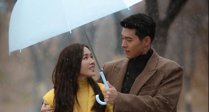 still shot from crash landing on you: man and women look into each other's eyes under an umbrella