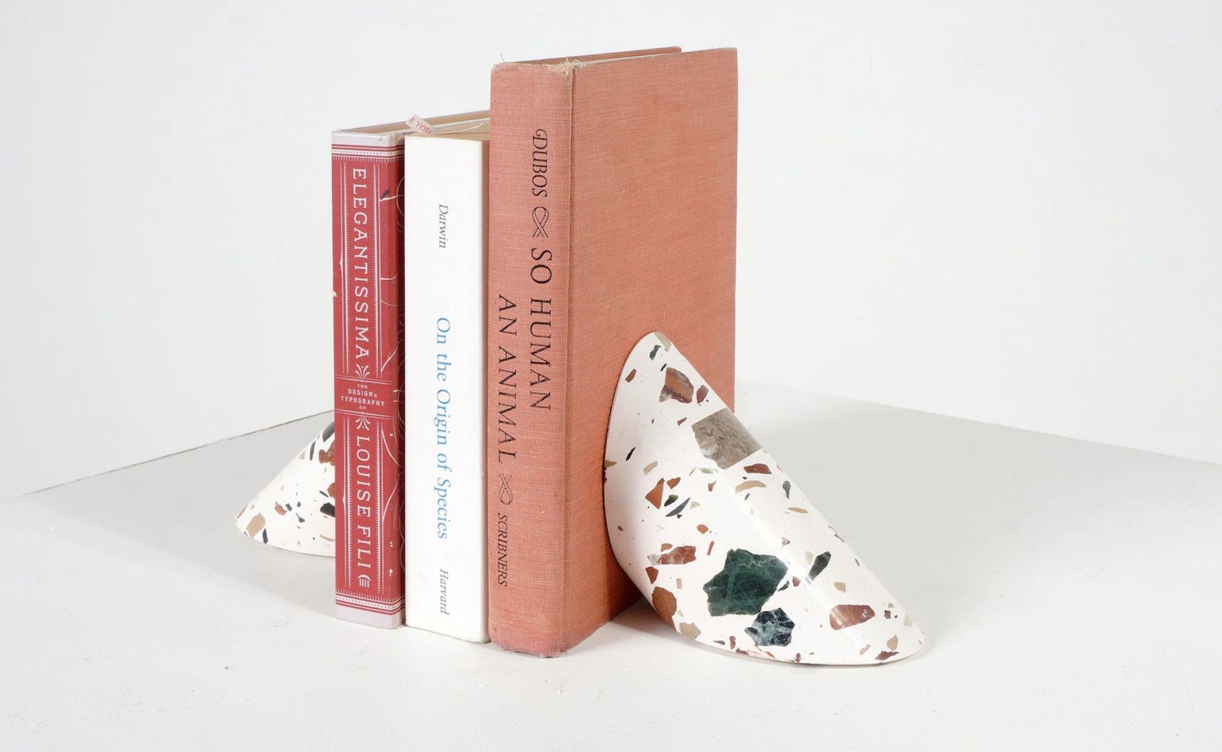 single terrazzo bookend in white with neutral-colored flecks. the bookend is in the shape of a half moon. 