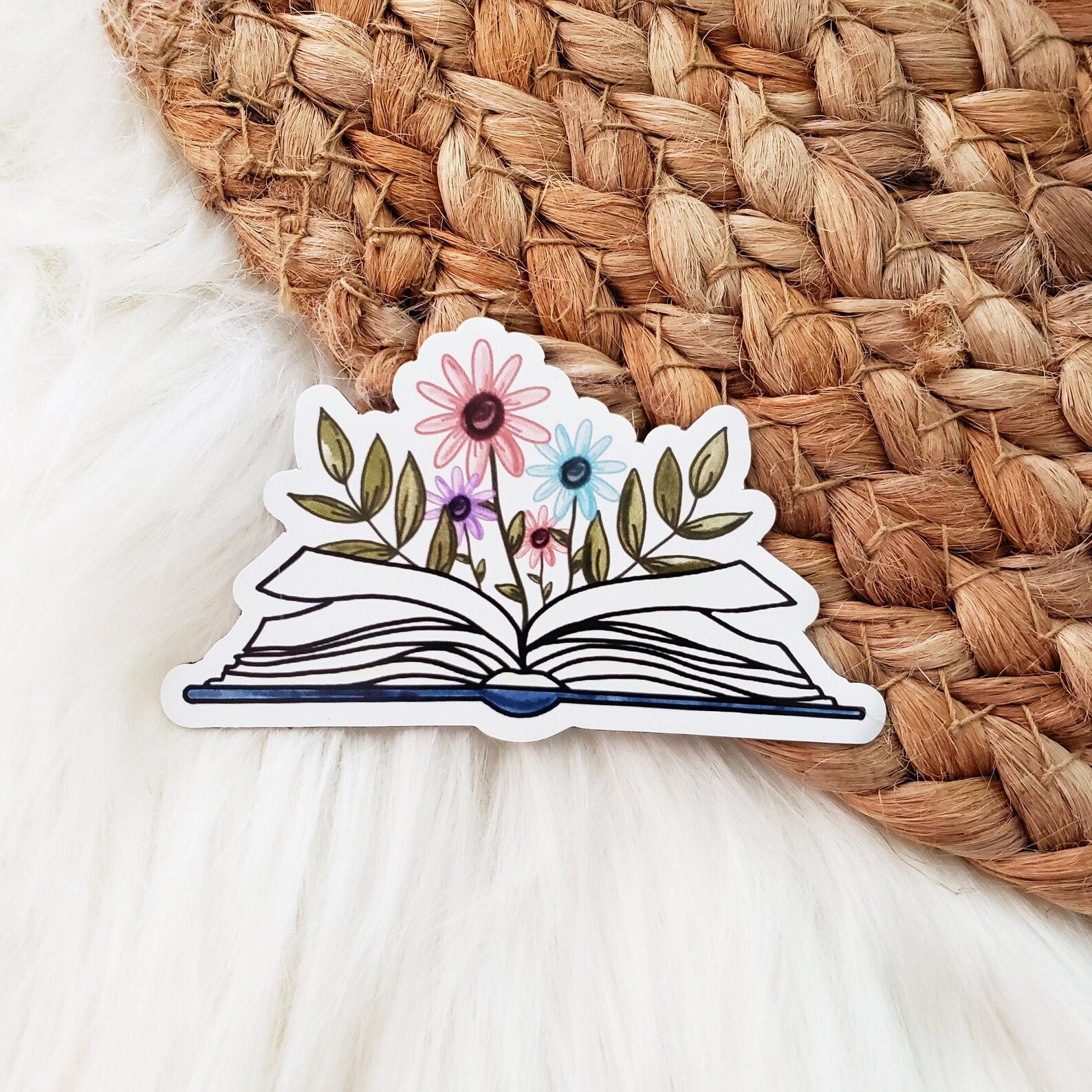 a magnet featuring an open book with pink, blue, and purple flowers growing from the center