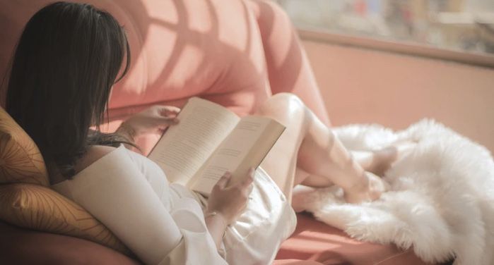 a woman reading a book sitting on a pink couch