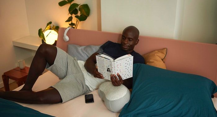 Image of a Black man reading a book on a bed.