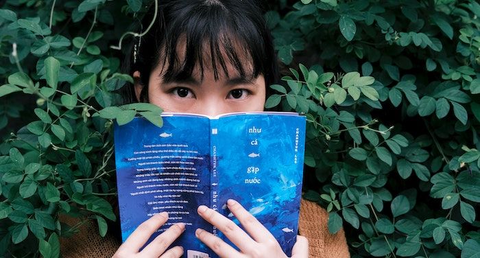 Image of an Asian woman with a book in front of her face