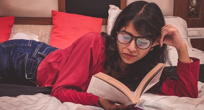 Image of a dark haired woman reading on a bed