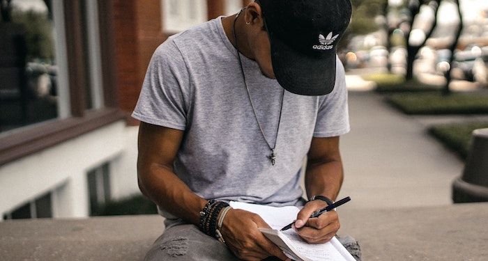 Image of brown skinned person with notebook and pen sitting outside