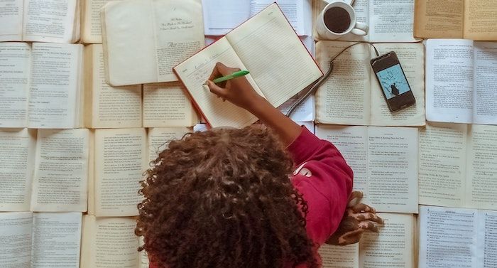 Image of top of woman's head who is on top of a pile of books and writing in a notebook