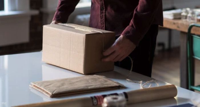 person packing up a cardboard box, assorted packing supplies strewn next to them on a white table