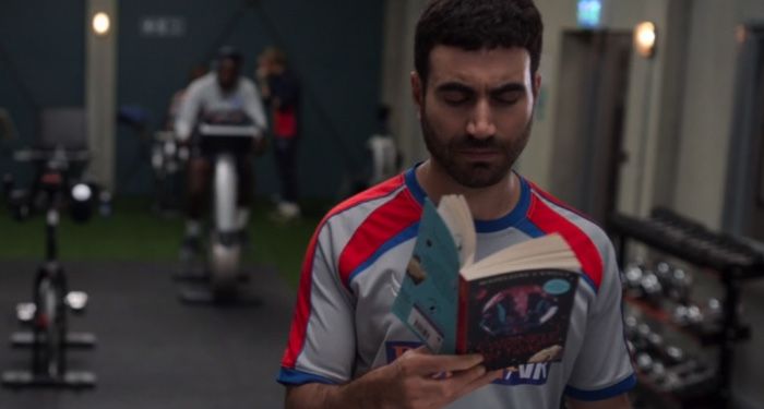 in a still frame from Ted Lasso Roy is reading a copy of A Wrinkle in Time