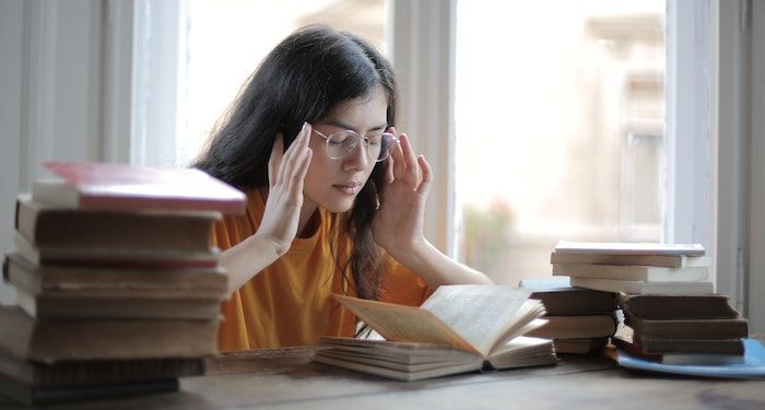 woman holding her temples surrounded by books