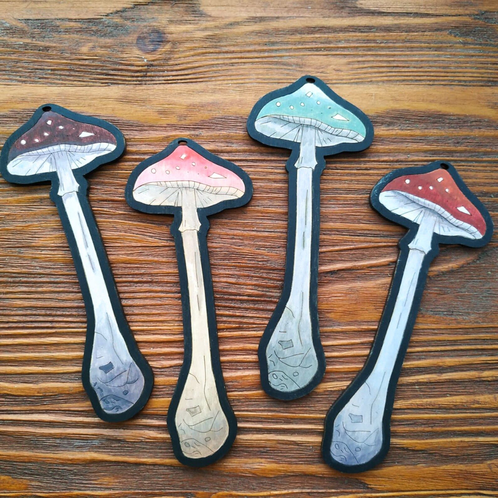Image of four wooden mushroom bookmarks, one each in purple, pink, green, and red. 