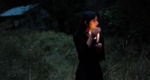 woman in a black dress holding a candle in a dark field