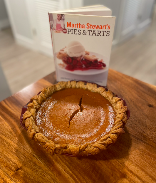 Pumpkin pie with pastry leaves around rim and a crack down the middle, with Martha Stewart's New Pies & Tarts cookbook