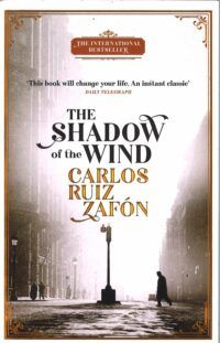Book cover for The Shadow of the Wind, showing a black and white image of a man crossing an empty street with a lamppost in the centre. A white light shines from the end of the street so the buildings on each side are indefinite.