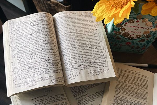 Open, annotated book lying open beside a vase of sunflowers. Photograph by the author of this piece, Leah von Essen.