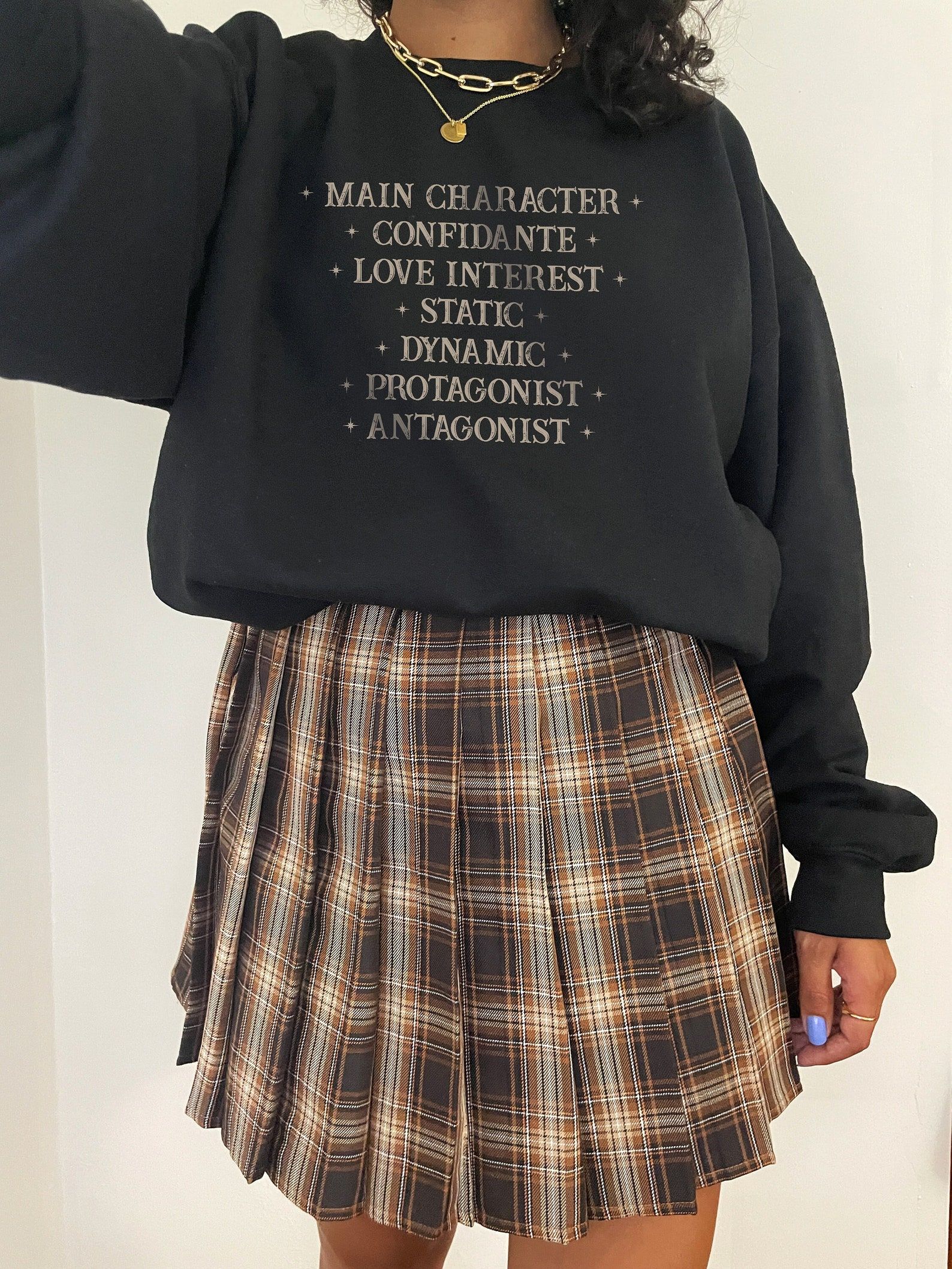 A black sweatshirt with gold script listing "main Character, Confidante, love interest, states, dynamic, protagonist, antagonist"