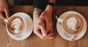 a pair of clasped hands between two coffee cups in saucers