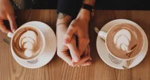 a pair of clasped hands between two coffee cups in saucers